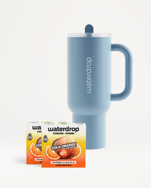 Modrý termohrnček Waterdrop s viečkom a slamkou umiestnený vedľa dvoch krabičiek príchute Cola Orange na bielom pozadí.