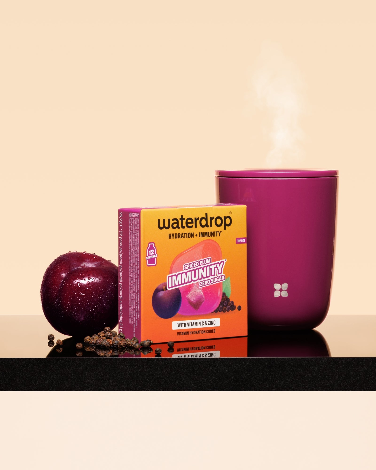 Krabica Waterdrop na podporu imunity vedľa slivky a horúcej ružovej šálky na čiernom povrchu.